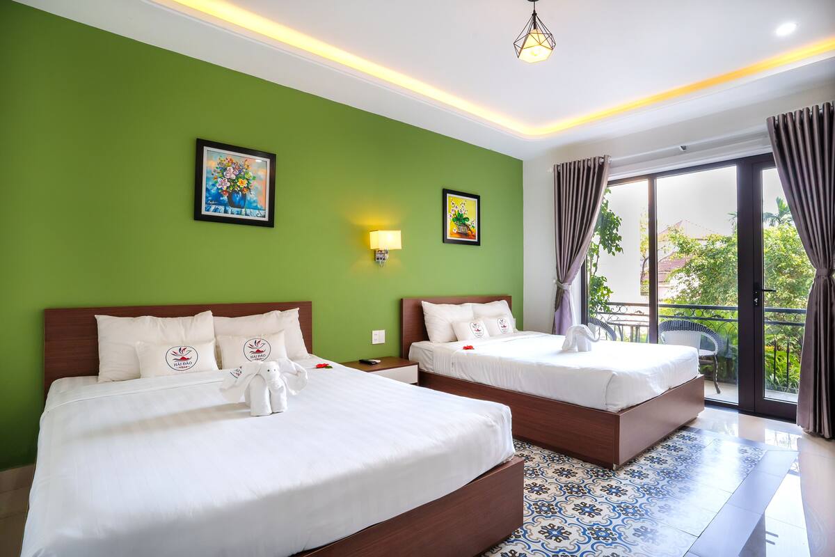 A hotel room with two beds, green walls, artwork, a balcony with curtains, and a tiled floor.