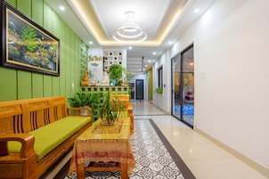 Un pasillo con un banco de madera, una mesa con mantel estampado y una pared verde con un cuadro enmarcado.