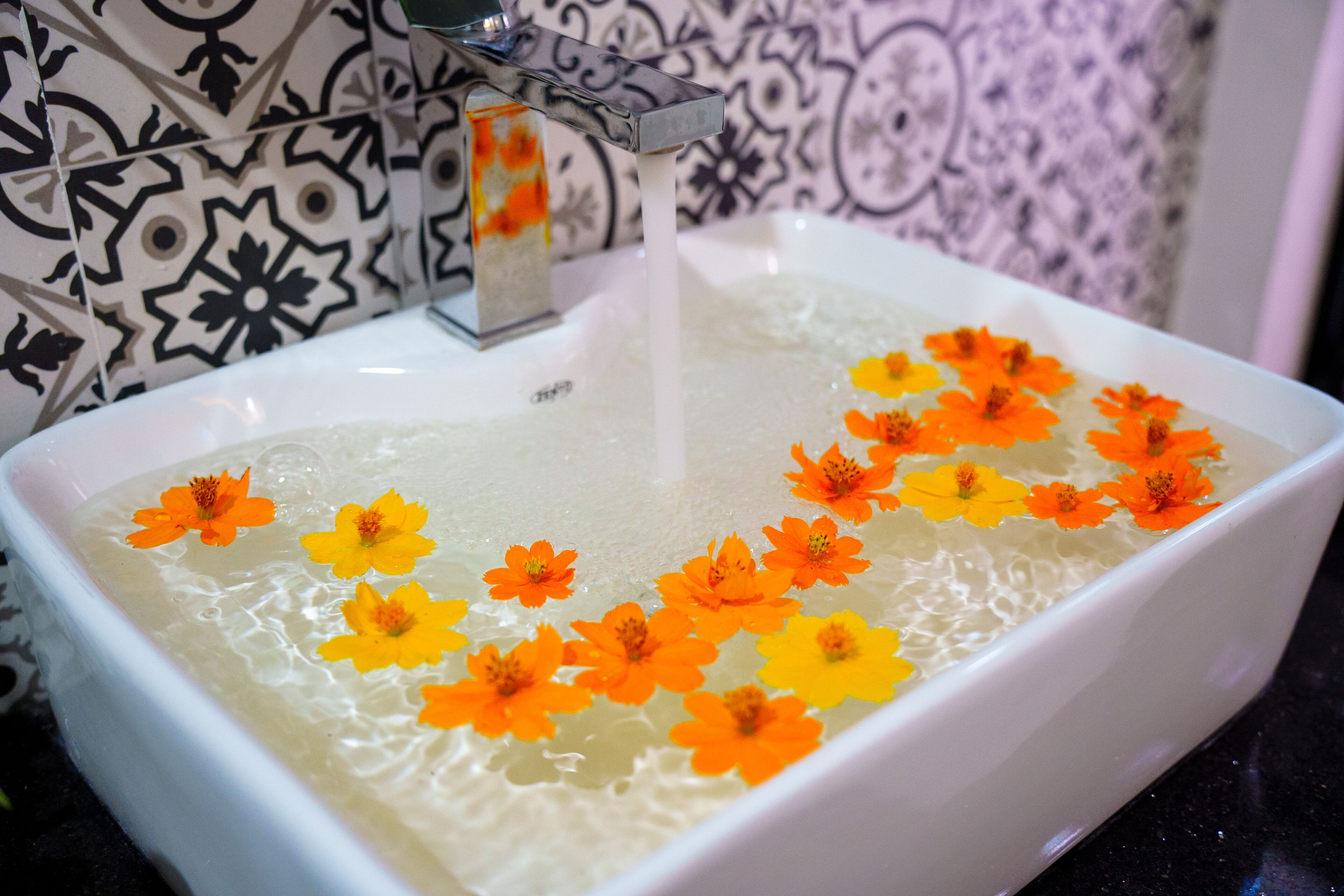 A white rectangular sink with a faucet, filled with water and floating flowers.
