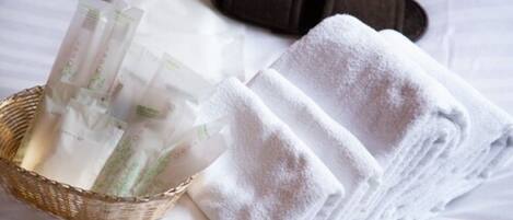 A bed with white linens, a basket of toiletries, and a black pillow.