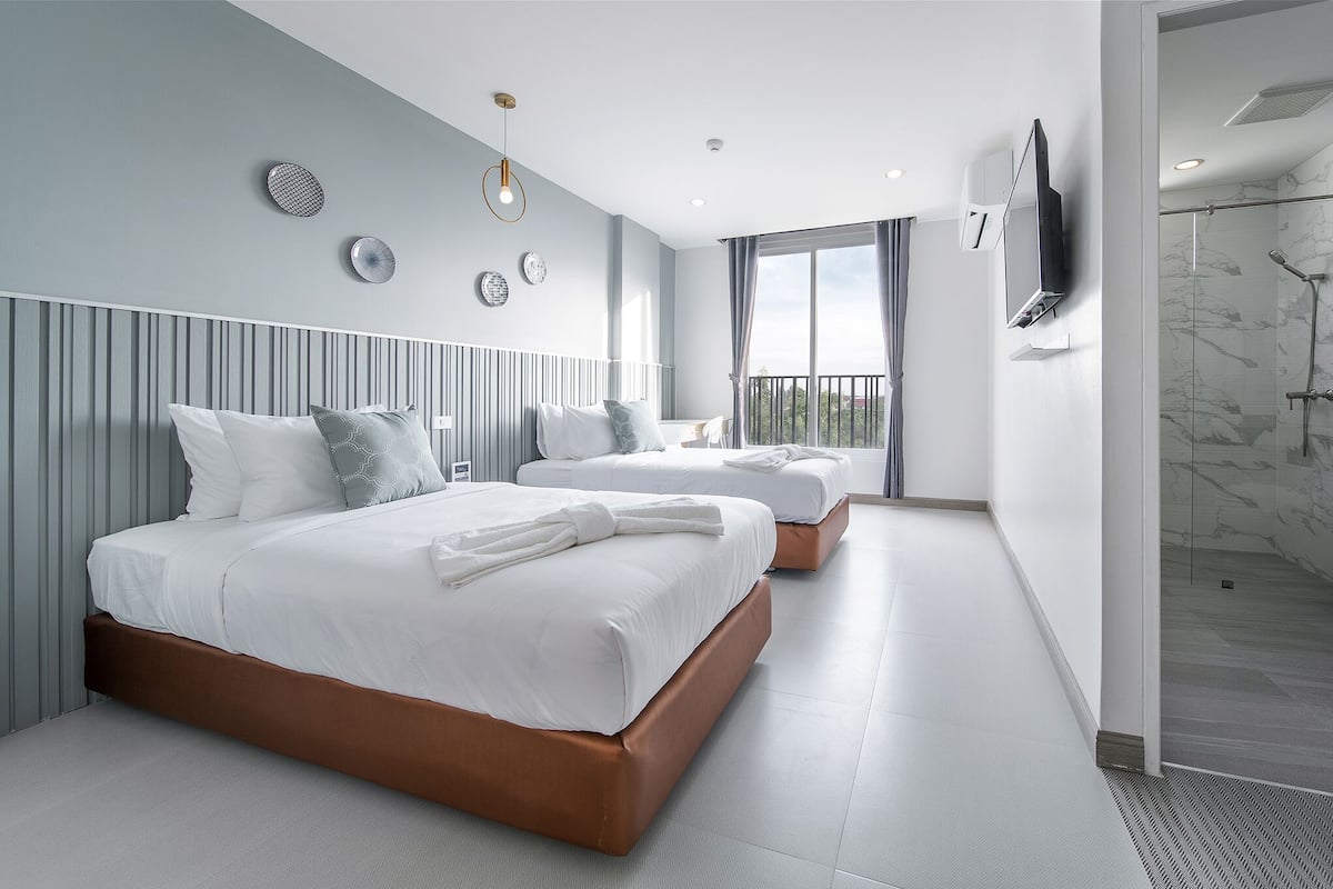 A modern hotel room with two beds, a large window, and a shower area.