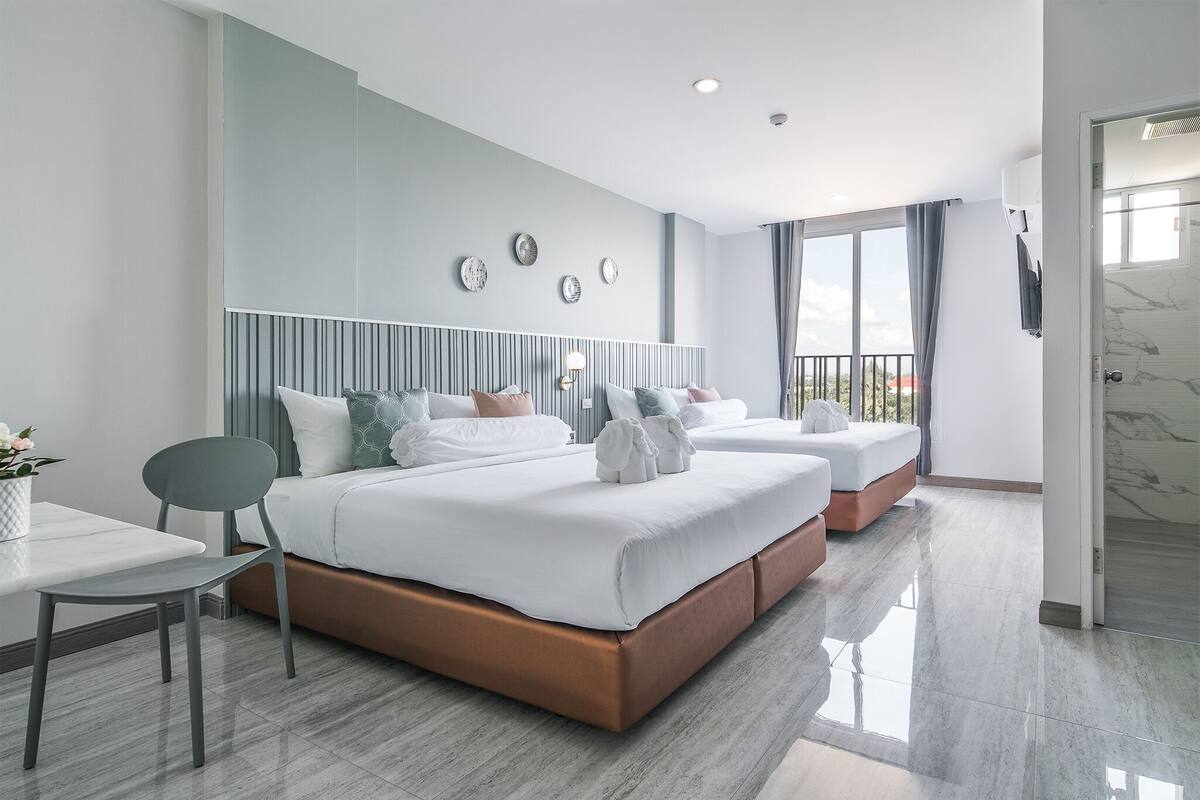 A modern hotel room with a large bed, a small table, and a chair. There are decorative wall plates above the bed and a balcony with curtains.
