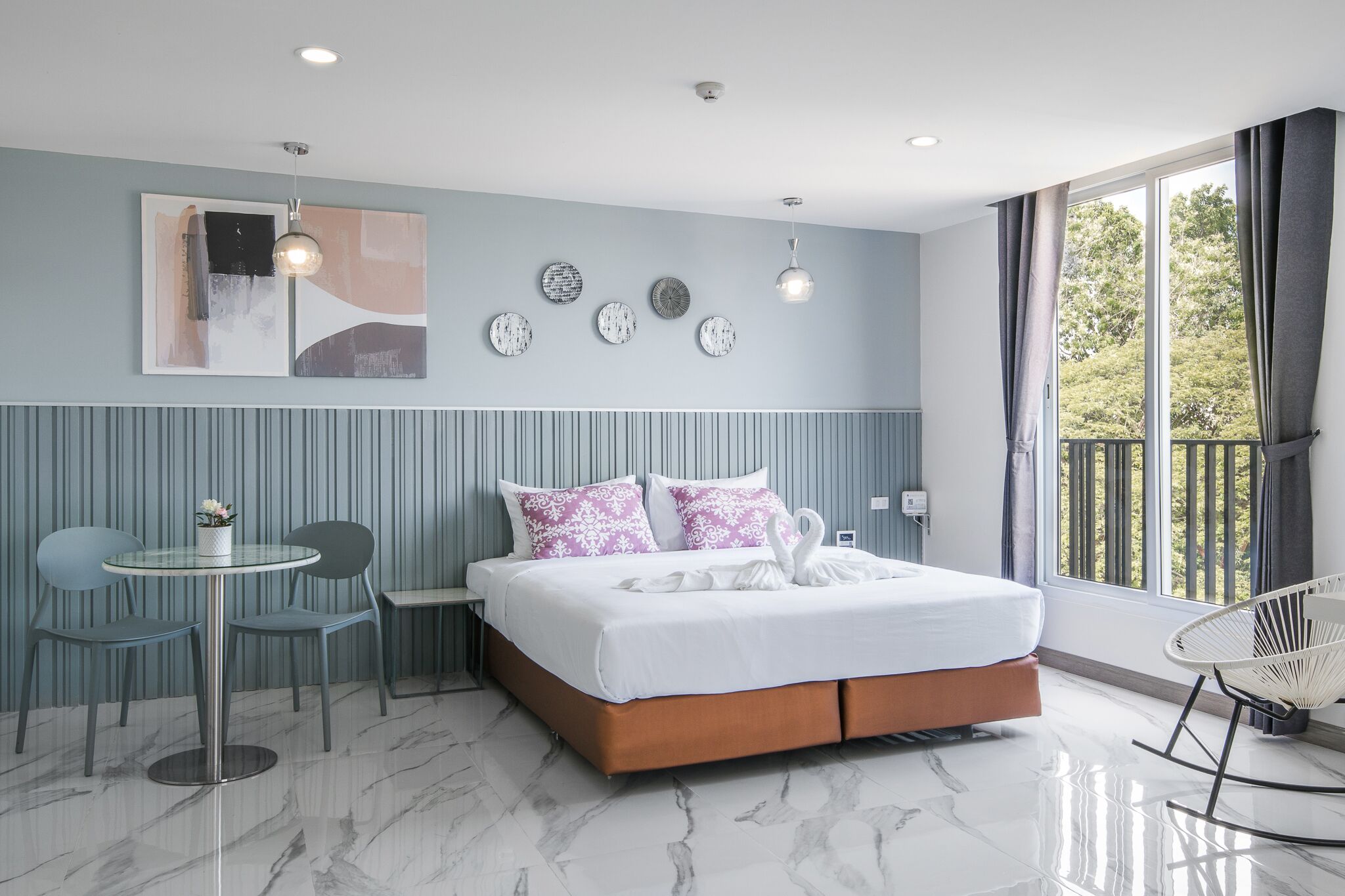 Un dormitorio moderno con una cama grande, una mesita redonda pequeña, dos sillas y vistas a zonas verdes por la ventana.