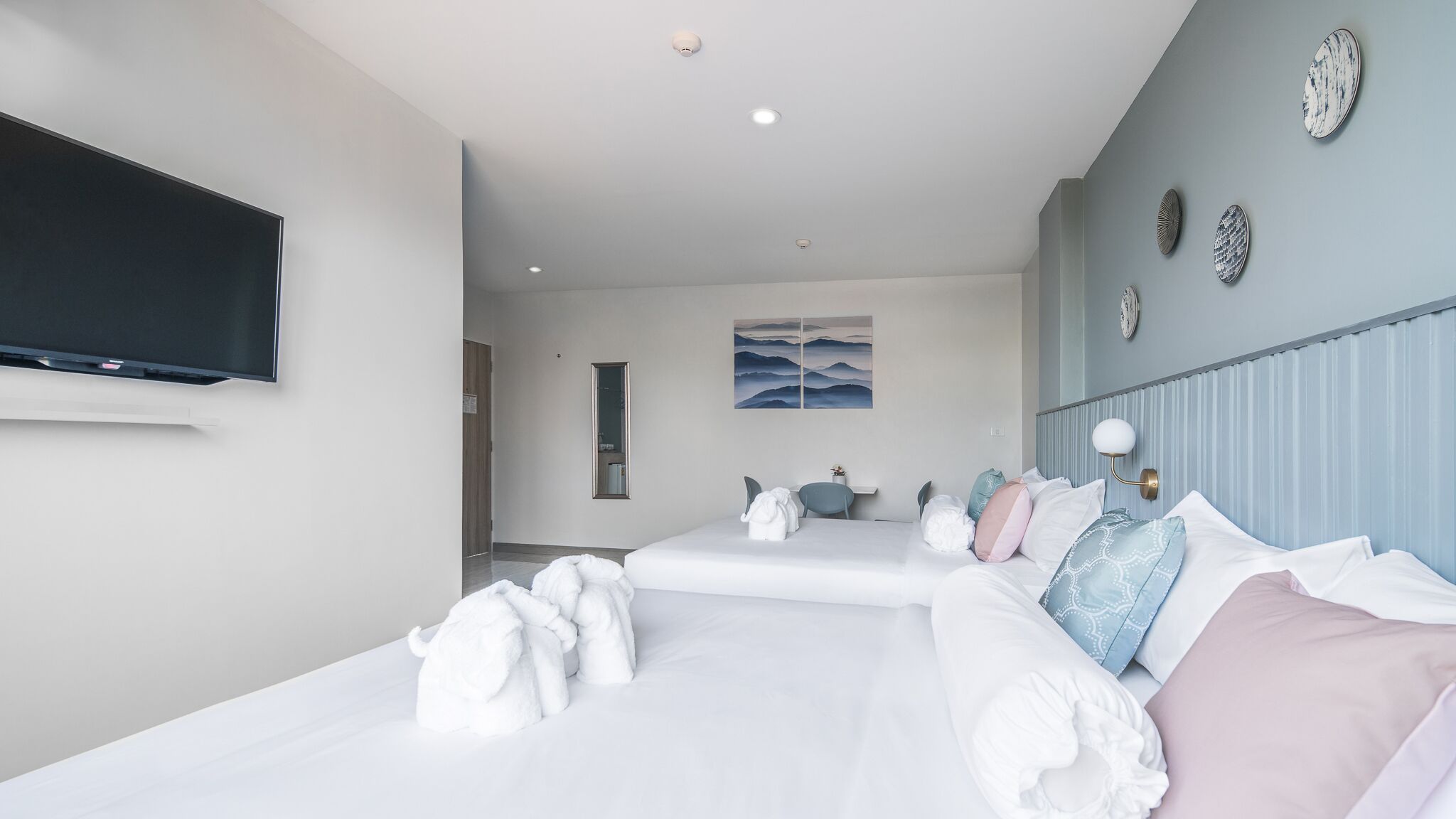 A hotel room with two beds, a flat-screen TV, a painting, and a mirror.