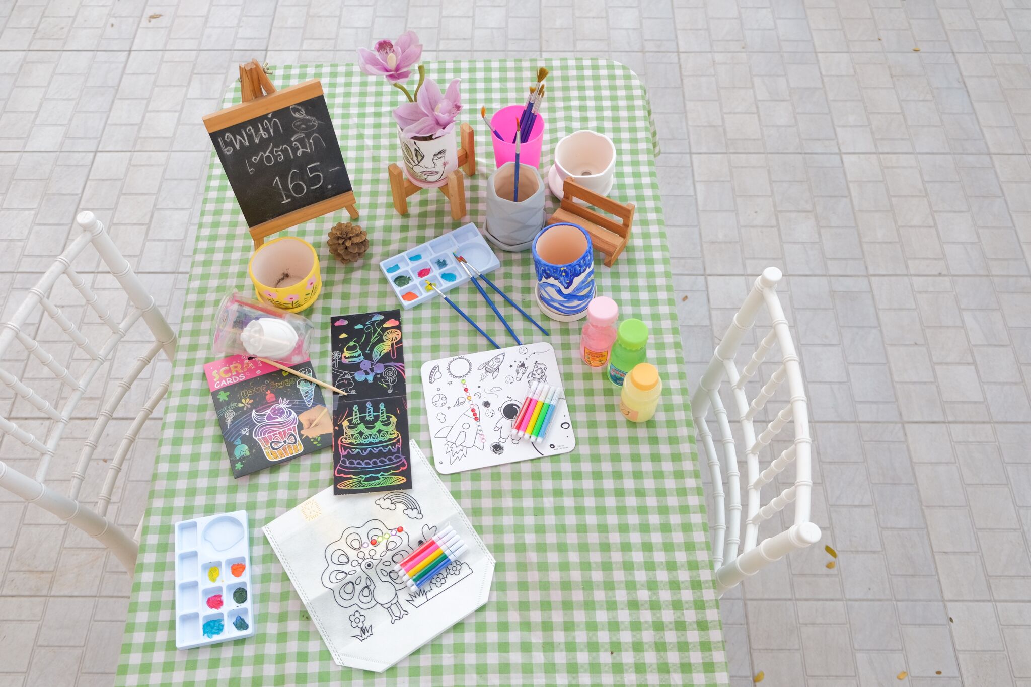 Una mesa dispuesta con material de arte, incluyendo pintura, pinceles y libros para colorear, sobre un mantel a cuadros.