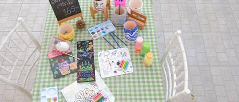 Una mesa dispuesta con material de arte, incluyendo pintura, pinceles y libros para colorear, sobre un mantel a cuadros.