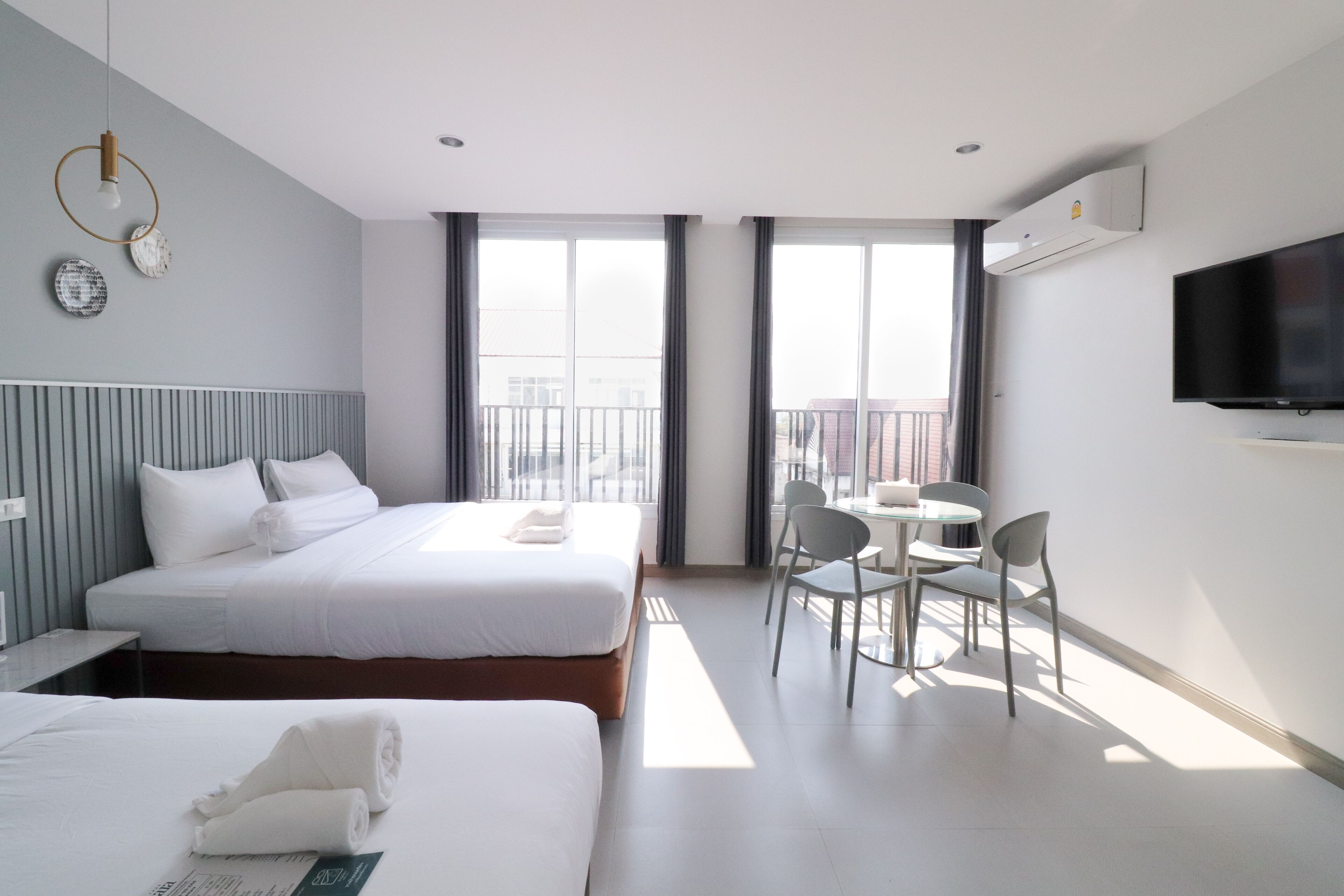 Ein Hotelzimmer mit zwei Betten, einem Esstisch mit Stühlen, einem Fernseher und großen Fenstern.