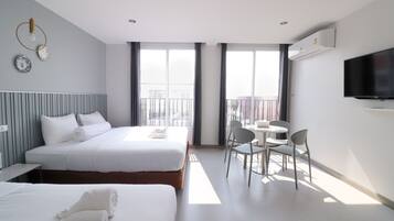 Ein Hotelzimmer mit zwei Betten, einem Esstisch mit Stühlen, einem Fernseher und großen Fenstern.
