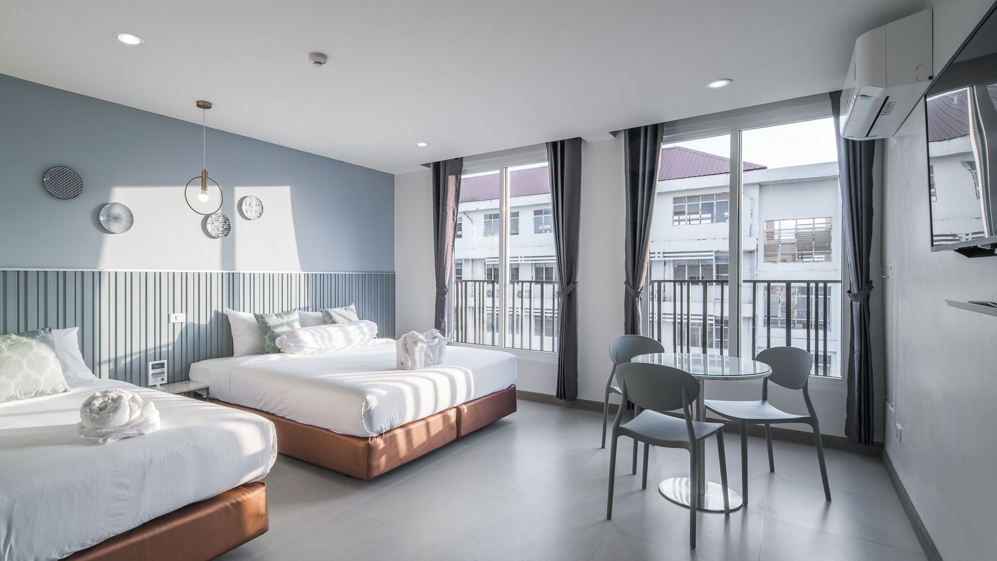 A modern hotel room with two beds, a balcony with a view, and a small dining area.