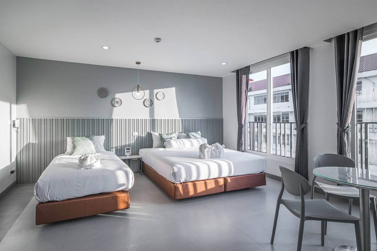 A modern hotel room with two beds, a glass table, and a view of the city.