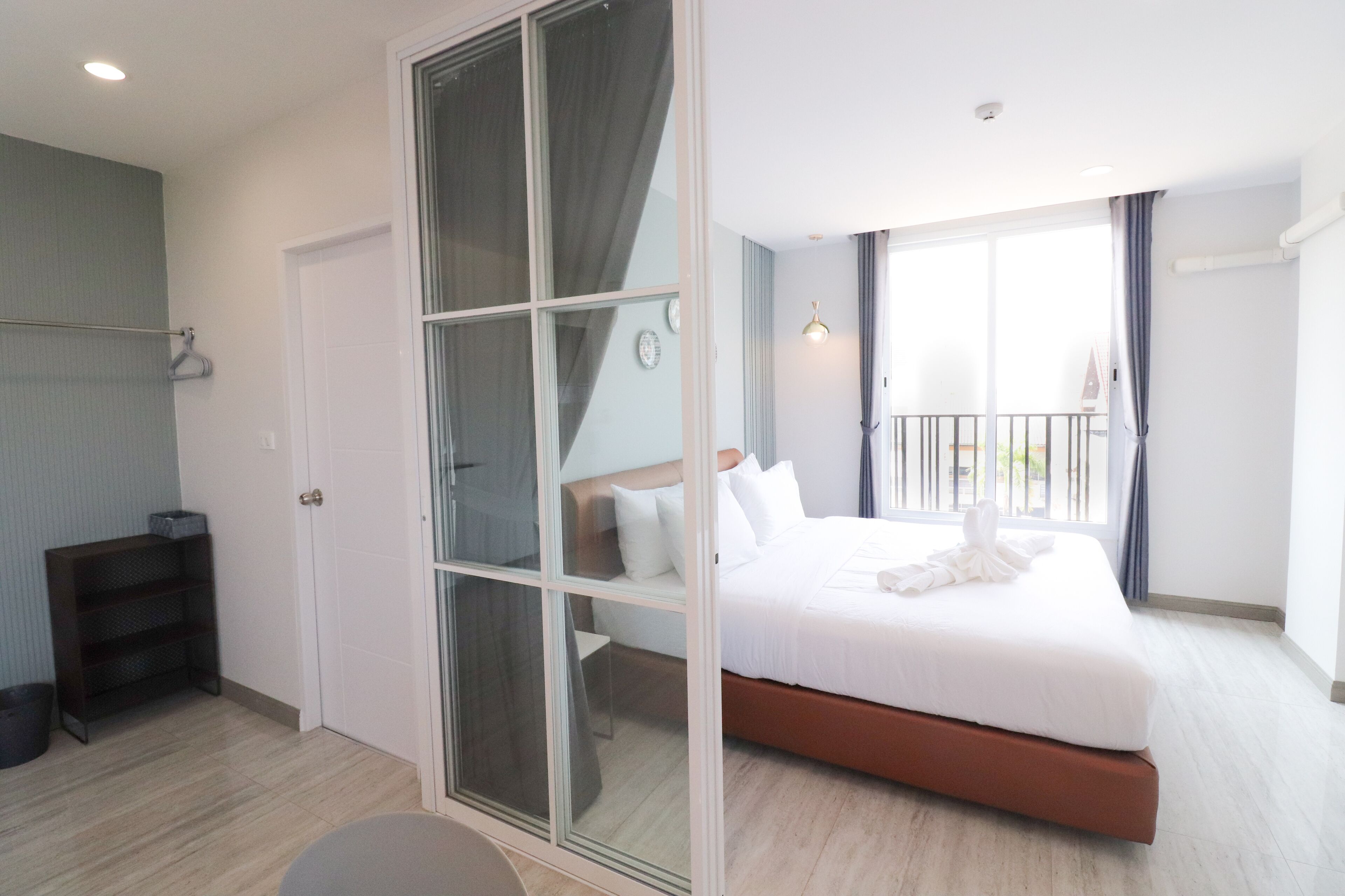 Una habitación de hotel moderna con una cama grande, un ventanal corredero que da a un balcón y una pequeña zona de estar.