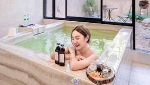 Une personne se détend dans une piscine intérieure moderne, avec vue sur un jardin et un espace patio.