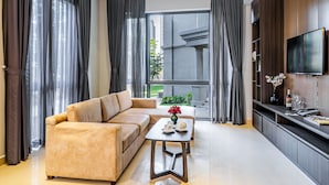 A modern living room with a beige sofa, a glass coffee table, and a flat-screen TV mounted on a wooden cabinet. - The Cap Hotel (Ho Chi Minh City)