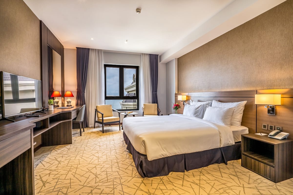 Quarto de hotel com cama, escrivaninha, cadeira e televisão.