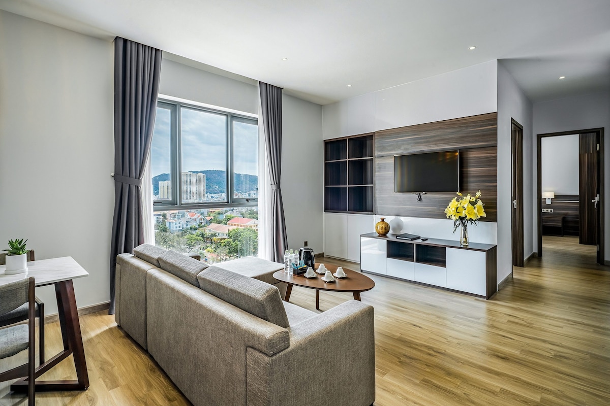 A modern living room with a sofa, a dining table, and a TV mounted on a wall.