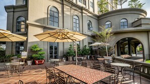 An outdoor patio with tables and chairs, surrounded by a building with large windows and a curved facade. - The Cap Hotel (Ho Chi Minh City)