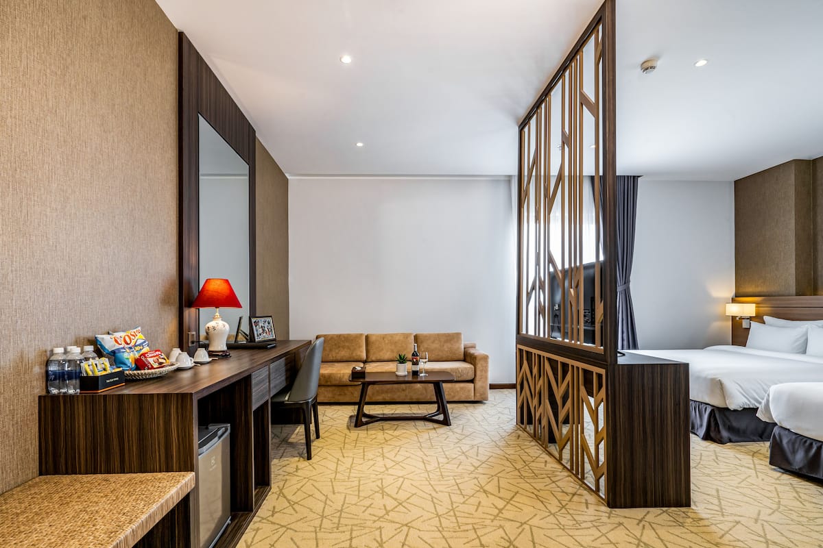 Quarto de hotel com sofá, escrivaninha com luminária, cama e um espelho grande.