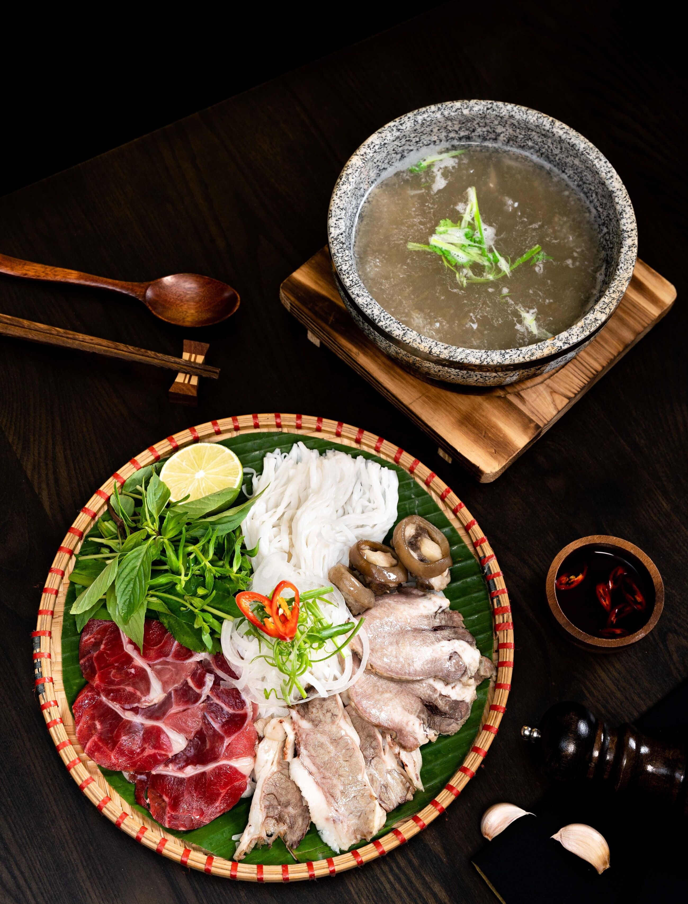 A dining table with a plate of sliced meats, a bowl of soup, and condiments.