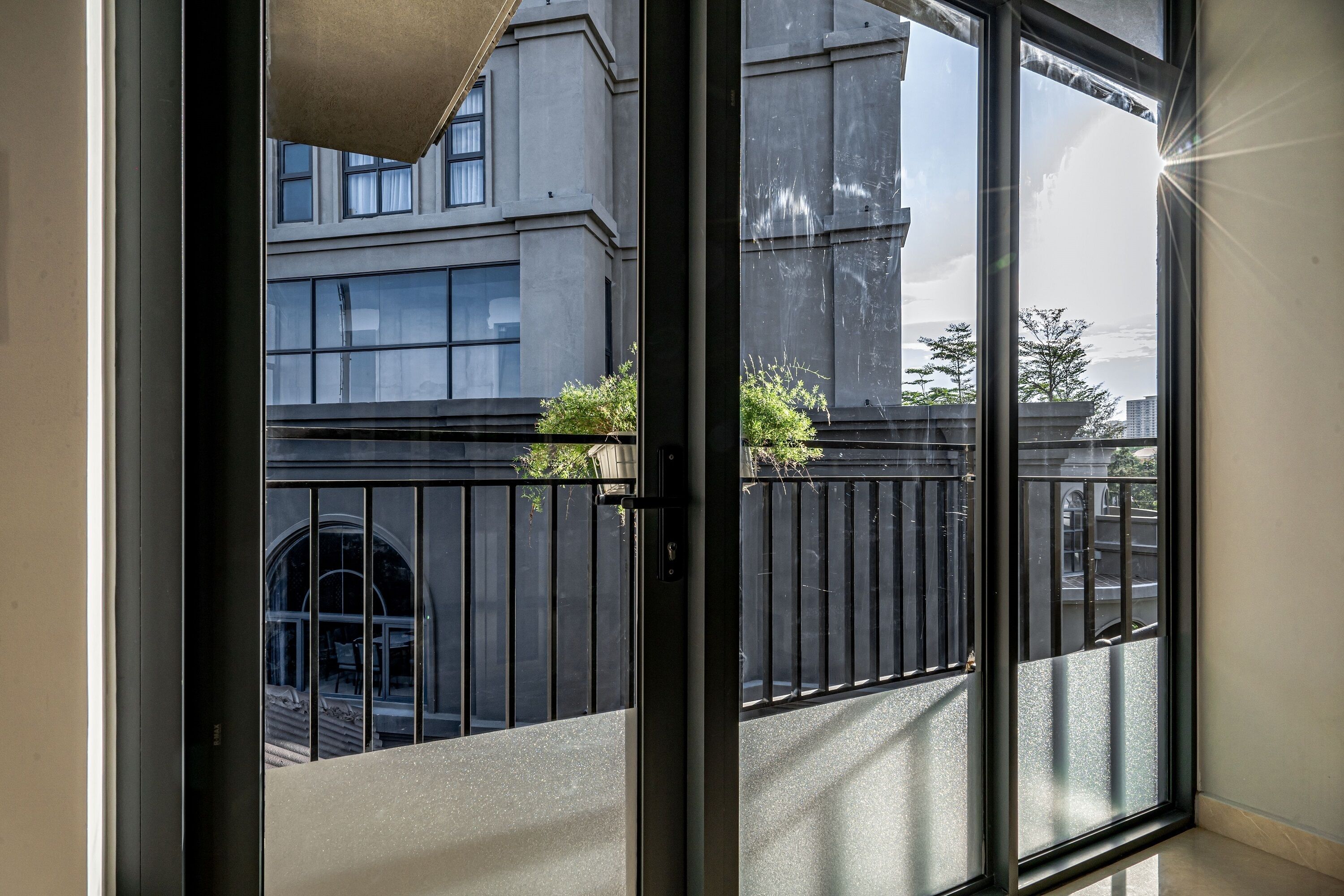 A view from a balcony with a metal railing, looking out at a building with large windows and a fence.