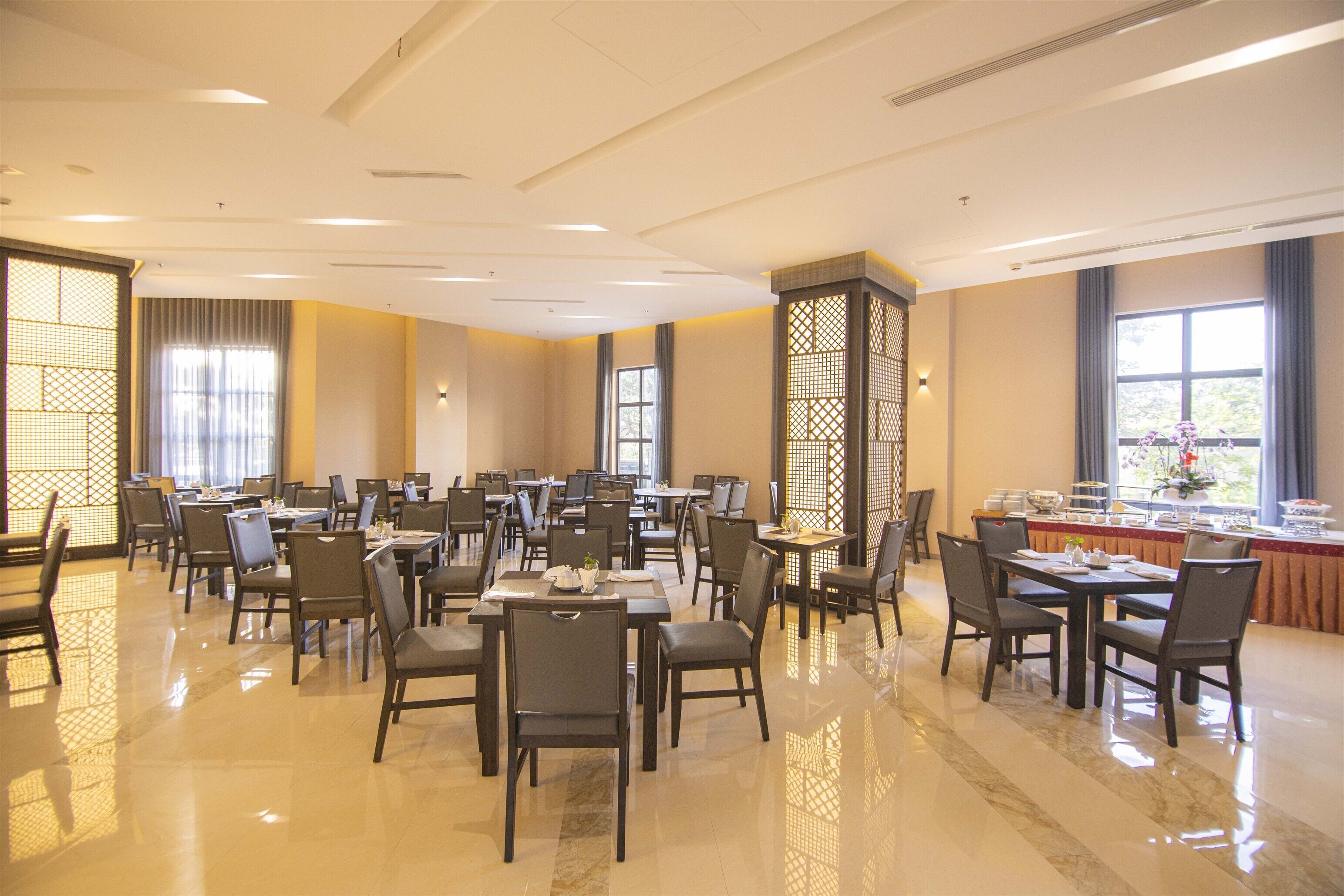 Un comedor amplio con varias mesas y sillas, ventanas grandes con cortinas y un separador decorativo con celosía.
