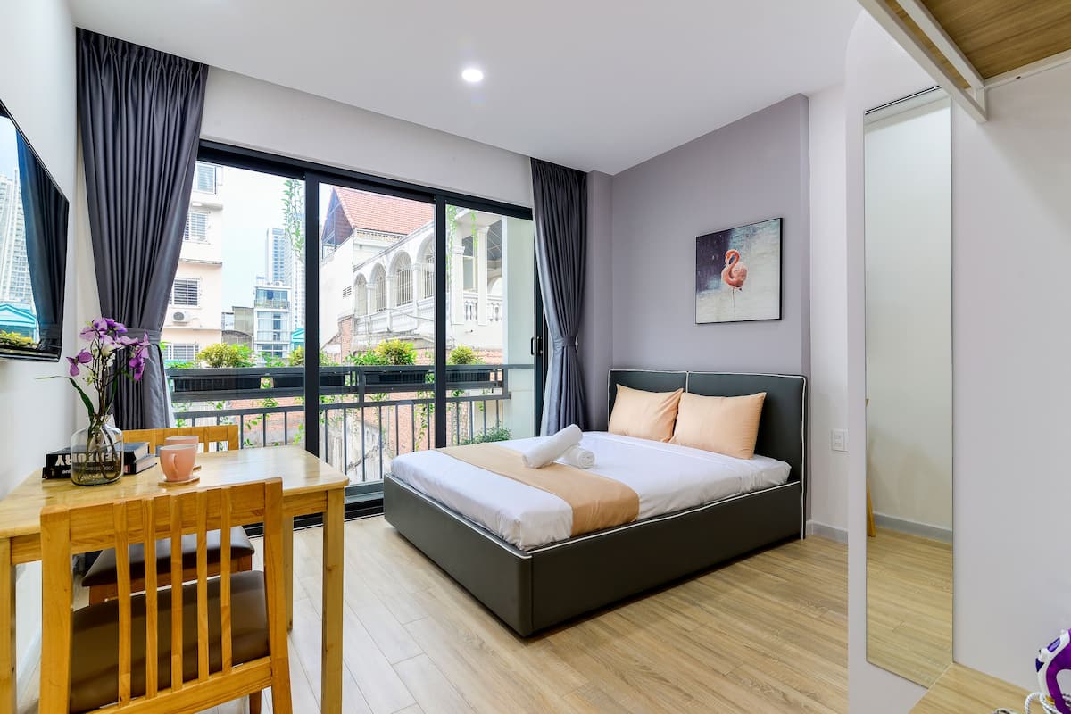Un dormitorio moderno con una cama grande, una mesa de madera y vistas a edificios a través de un ventanal.