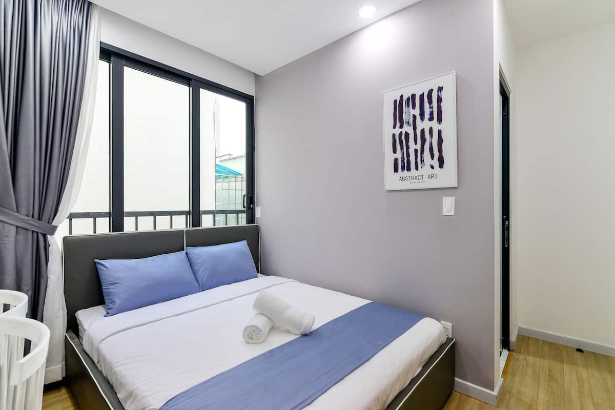 Una cama bien hecha con ropa de cama azul y blanca, una toalla blanca y una obra de arte abstracta enmarcada en la pared.
