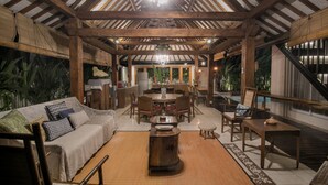 A spacious indoor area with a high ceiling, wooden beams, a central dining table surrounded by chairs, and a sofa with cushions. - Villa D'Kali 999 (Seminyak)