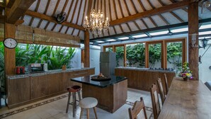 A spacious kitchen with wooden cabinets, a central island, and a dining area with a long wooden table. - Villa D'Kali 999 (Seminyak)