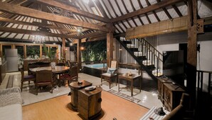A spacious living area with a high ceiling, wooden beams, a dining table, sofas, and a staircase leading to an upper level. - Villa D'Kali 999 (Seminyak)
