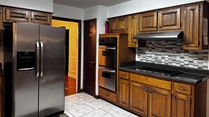 A kitchen with wooden cabinets, a stainless steel refrigerator, a tiled backsplash, and a black countertop.