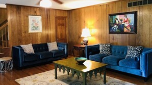 A living room with two blue sofas, a wooden ceiling fan, a lamp, and a painting on the wall.