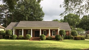 A two-story house with a front porch, a well-maintained lawn, and several small trees.
