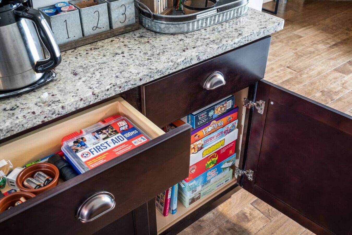 A kitchen with a granite countertop, a coffee maker, and a drawer containing board games.