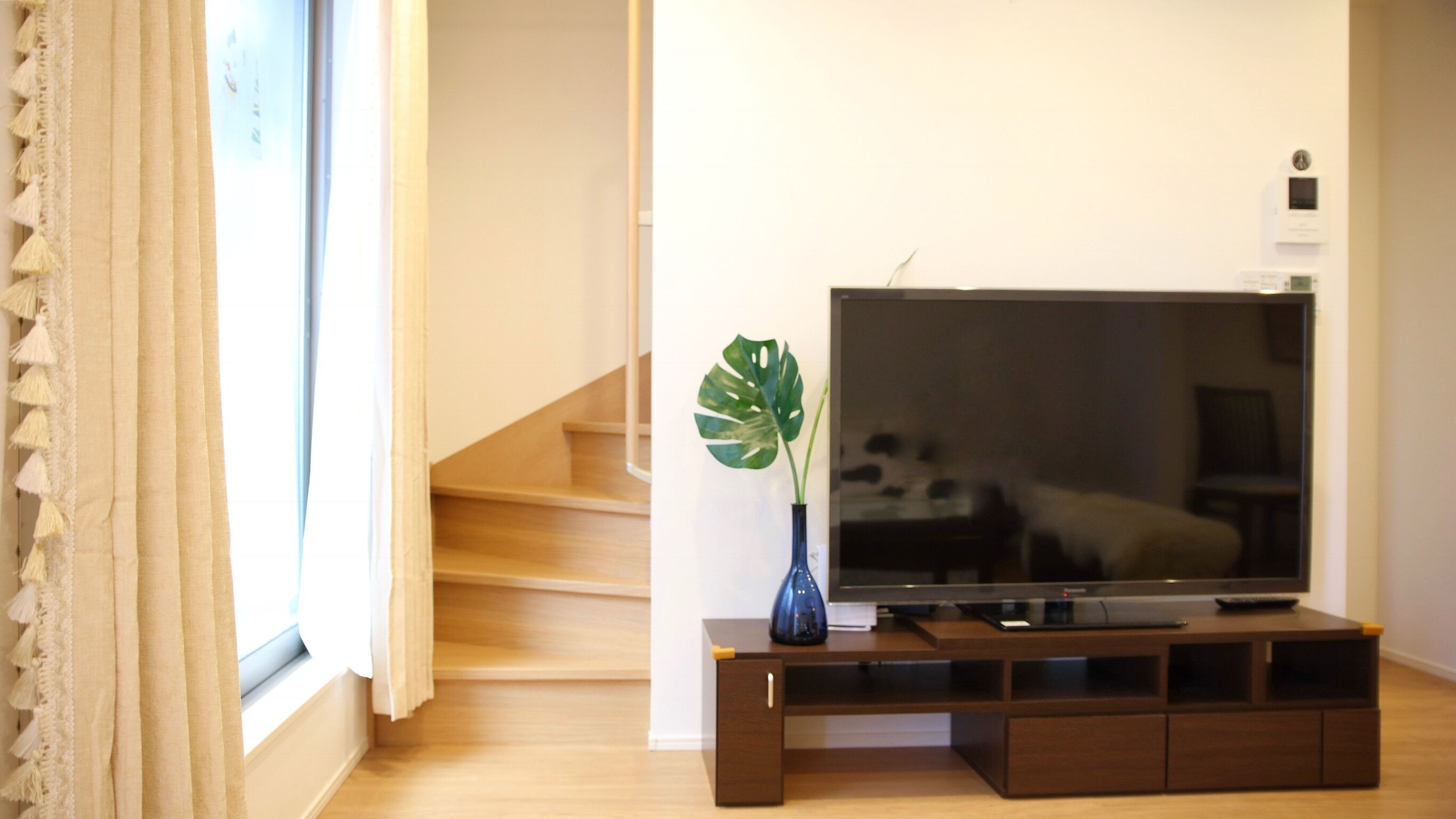 A living room with a TV on a wooden stand, a plant, and a staircase.