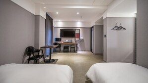 Habitación de hotel con dos camas, un escritorio, una silla, una mesita y un espejo.