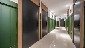Un pasillo de hotel con puertas verdes y negras, piso de baldosas y diseño moderno.