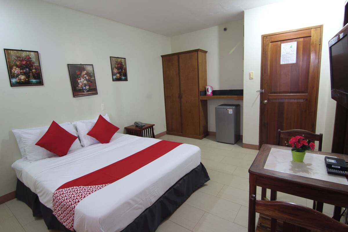 A hotel room with a bed, a desk, a chair, a wardrobe, and a refrigerator.