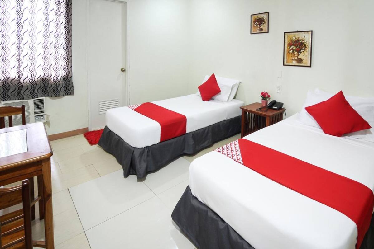 Habitación de hotel con dos camas, cada una con ropa de cama roja y blanca, una mesita de madera y una silla.