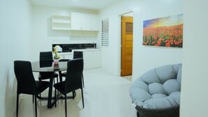 A modern kitchen with white cabinets, a dining table with black chairs, and a painting of a field of flowers on the wall. - Ljenj Apartelle (Mabalacat City)