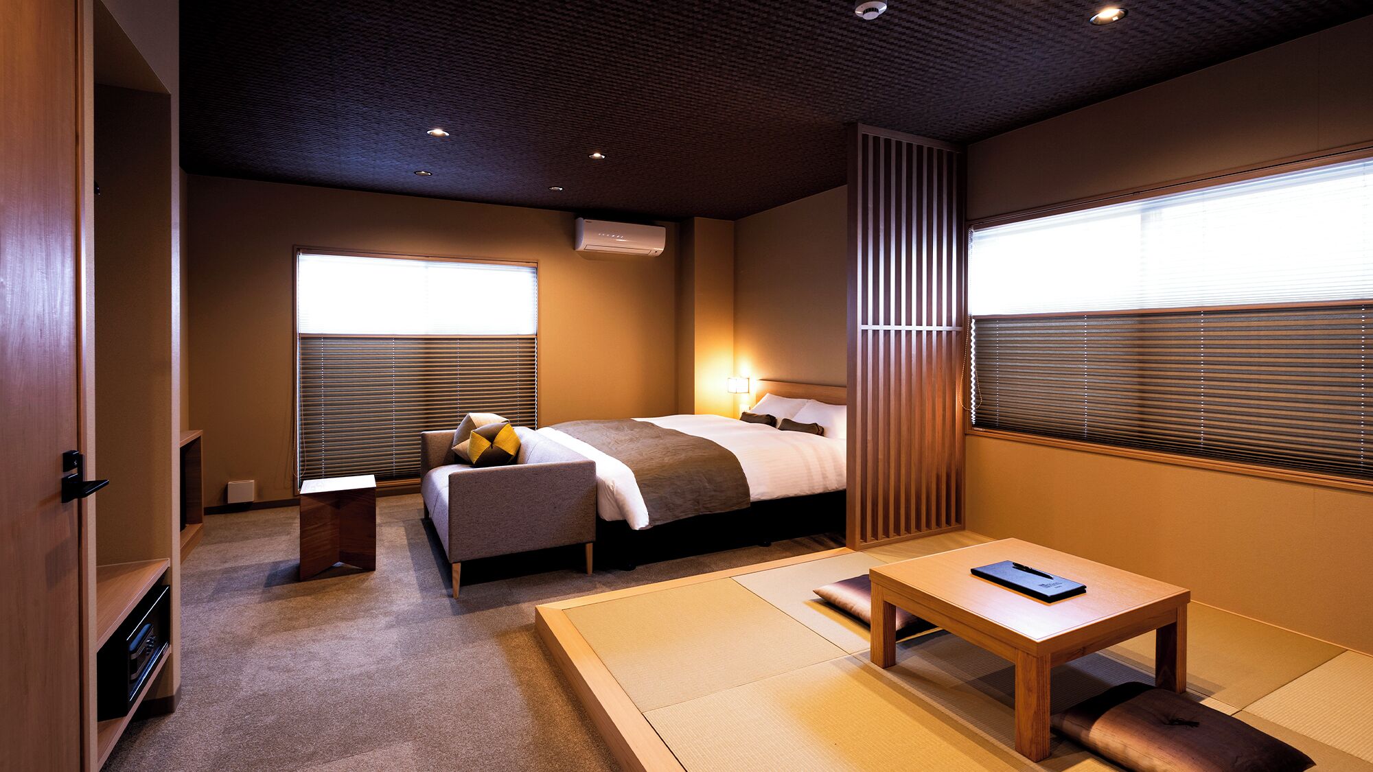 A hotel room with a bed, bedside table, and a window with blinds.