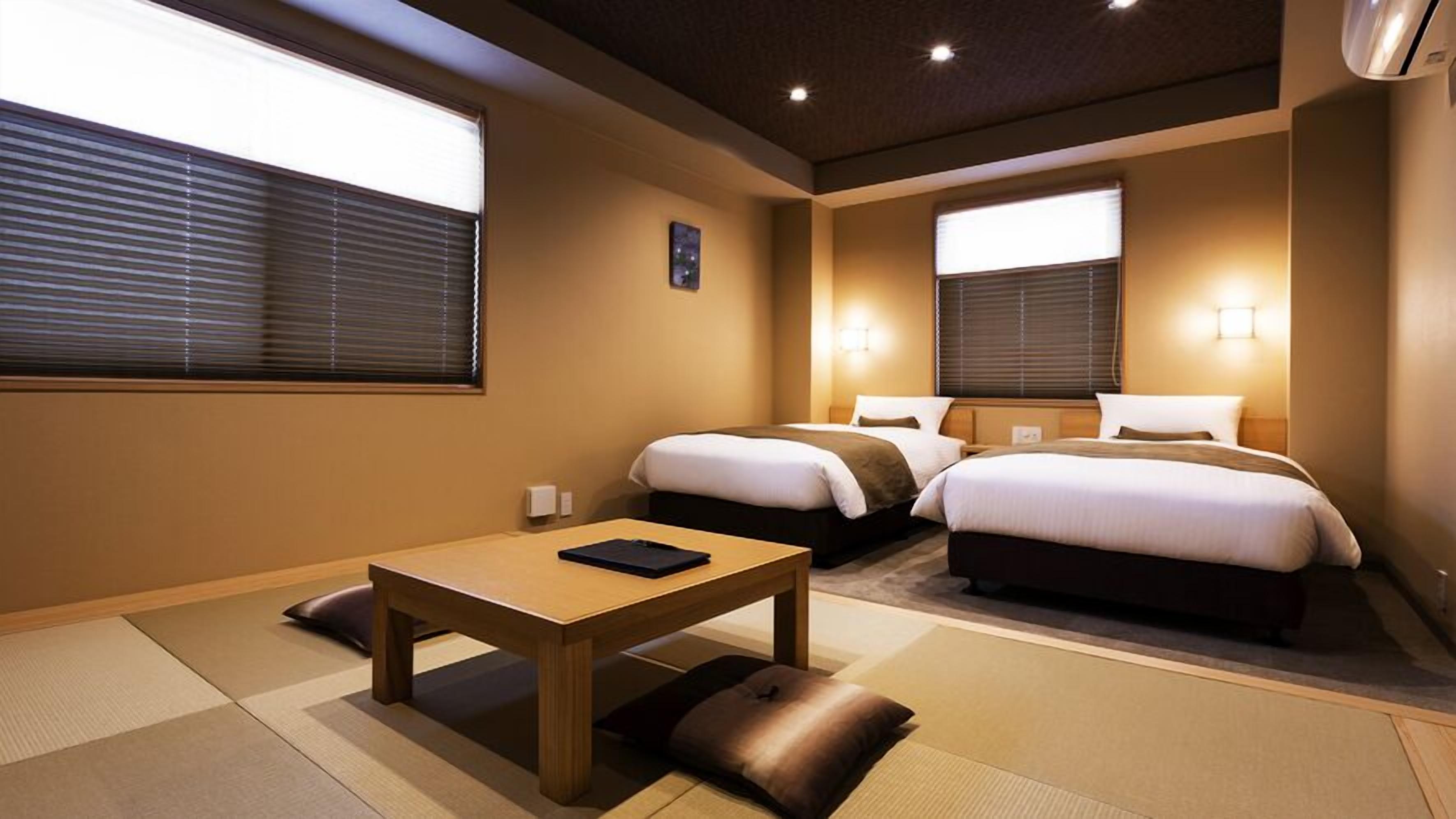 A hotel room with two beds, a small table, and a futon.