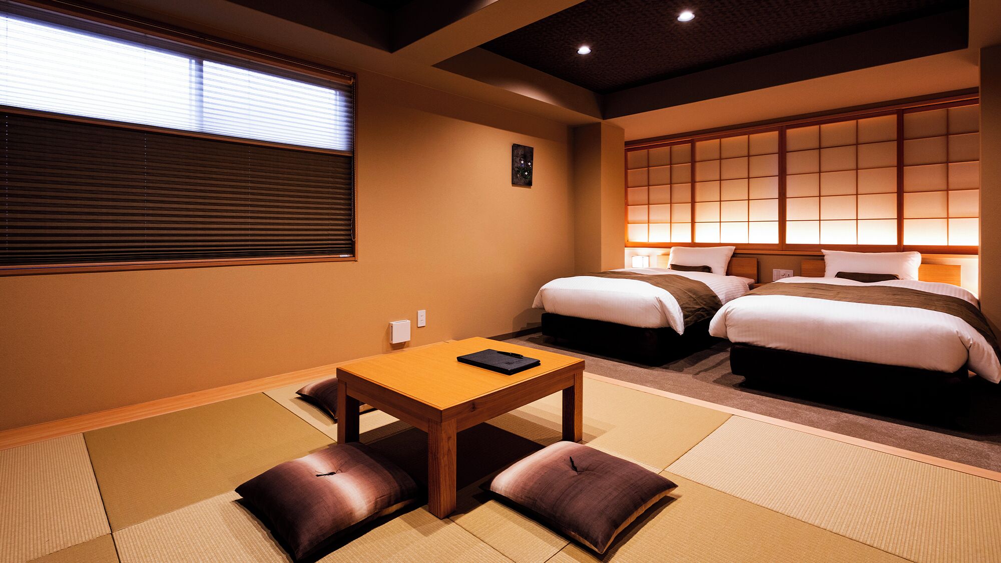 A hotel room with tatami flooring, a wooden table, two beds, and a sliding shoji screen.