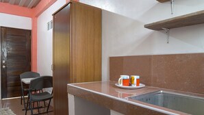 Una pequeña cocina americana con un lavamanos, un mueble de madera, dos sillas y una mesa pequeña con una taza y un platillo.