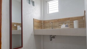 Un baño con un lavamanos blanco, un salpicadero de madera y un espejo, además de una ventana.