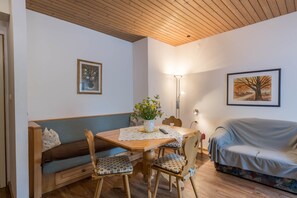 A cozy room with a wooden ceiling, a dining table with chairs, a sofa, and two framed pictures on the walls.