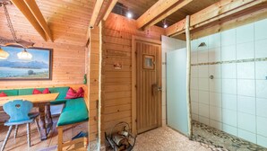 L’intérieur d’une cabane en bois, avec un banc, une table et une porte donnant accès à une zone douche.