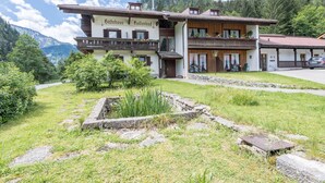 Un bâtiment de style chalet traditionnel, doté d’un balcon, d’un chemin en pierre et surplombant un paysage montagneux.