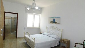 Un dormitorio con cama, mesita de noche, silla, un cuadro y una puerta que da al baño.
