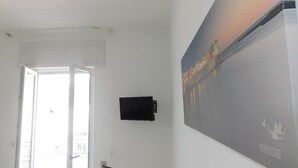 Una habitación con una puerta que da a un espacio exterior, un televisor montado y un cartel grande en la pared.