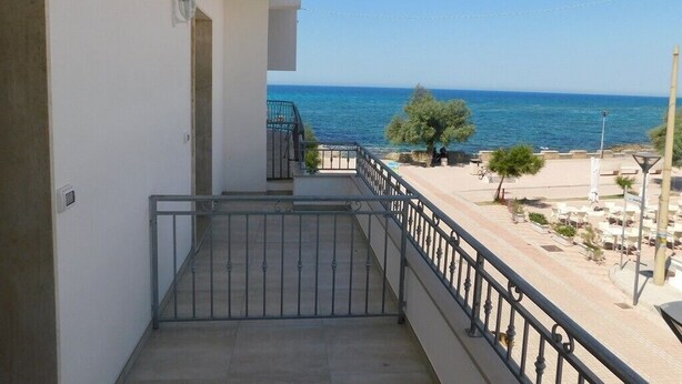 Un balcón con vista al mar, baranda de metal y una puerta que da a un espacio cubierto.